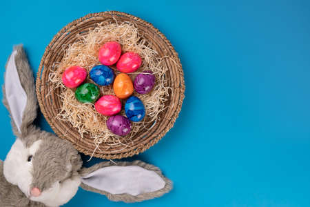 Easter bunny with colored eggs in a basket on a blue background. Easter concept. Copyspace.の写真素材