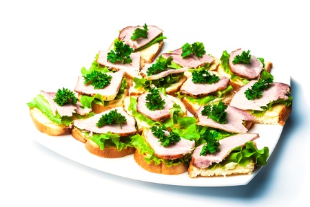Closeup of delicious ham and salad canapes sandwiches with parsley lying on a white plate.の写真素材