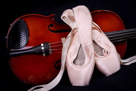 Ballet en pointe shoes resting against a violin on a black background.の写真素材