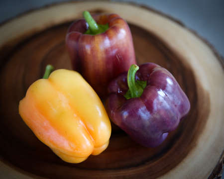 Multi colored heirloom bell peppers in yellow, red, and purple on a wood platter.