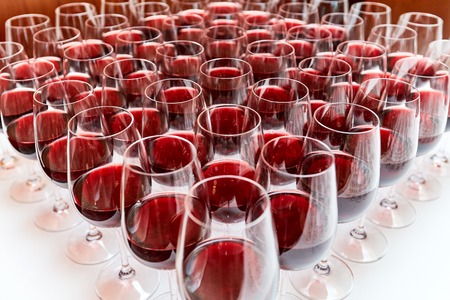 Glasses with red wine on a white table stand in the form of a triangleの写真素材