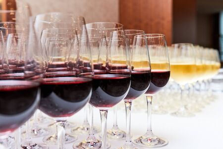 glasses with red and white wine on a white table stand in the form of a triangleの写真素材