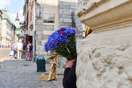 Lviv, Ukraine, June, 8, 2018. An old woman holds flowers of cornflowers in her hands in the street on a sunny dayの写真素材
