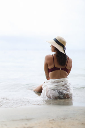 Young woman with bikini and hat looking left sitting at the beach at Bocas del Toro Panamaの写真素材