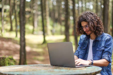 Young latin man sitting in the forest working with laptop freelancing looking laptop focused at Costa Rica.の写真素材