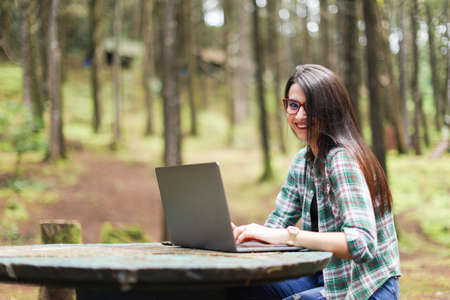 Young latin woman sitting in the forest working with laptop freelancing looking camera smiling at Costa Rica.の写真素材