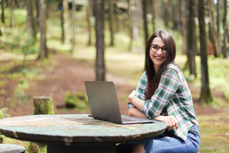 Young latin woman sitting in the forest working with laptop freelancing looking camera smiling at Costa Rica.の写真素材