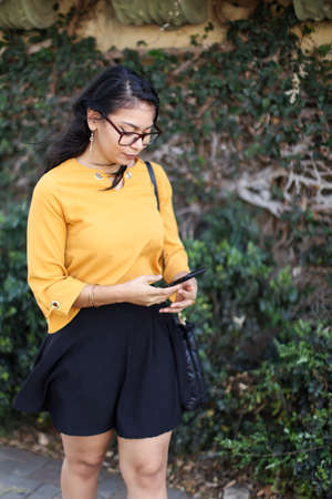 Young latin American brunette woman looking phone in front of a leaves background at Costa Ricaの写真素材