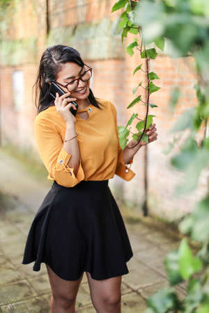 Young brunette Latin American woman talking on the phone touching plantの写真素材