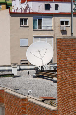 Satellite dish on the gravel roof of a building.の写真素材
