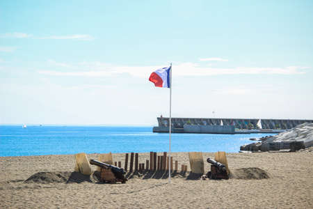 Malaga, Spain - October 26, 2014: French flag flies between two cannons on a beach next to the harbor. Historical reenactment of a Napoleonic corsair base.のeditorial素材