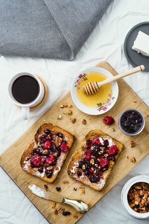 toasted bread with honey, cream cheese, red fruit jam and coffee, on table and woodの写真素材