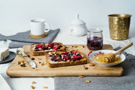 toasted bread with honey, cream cheese, red fruit jam and coffee, on table and wood