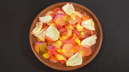 Aromatic rose petals on a wooden plate on dark backgroundの写真素材