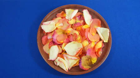 Aromatic rose petals on a wooden plate on blue backgroundの写真素材