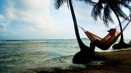 Lonely man watching the sunset sitting in the hammock on the beach