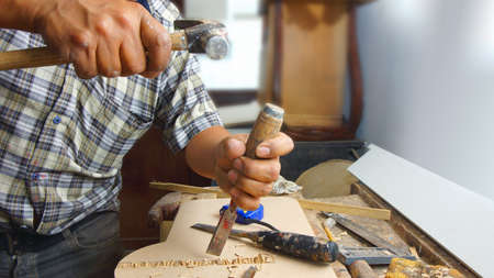 Carpenter hitting a chisel with a hammer modeling a wooden board on his desk