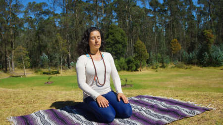 Young latin woman sitting meditating in the park on a blanket fabricの写真素材