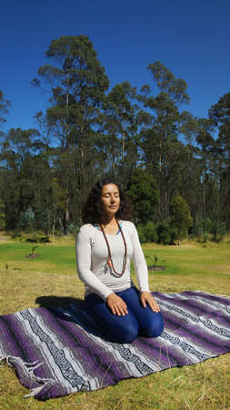 Young latin woman sitting meditating in the park on a blanket fabricの写真素材
