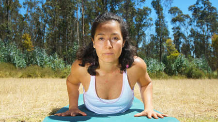 Young latin woman doing yoga in the park on yoga matの写真素材