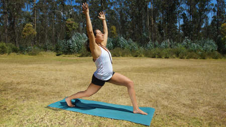 Young latin woman doing yoga in the park on yoga matの写真素材
