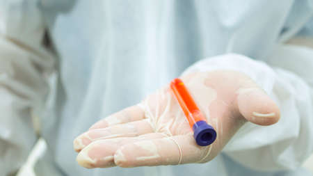 Doctor with white bioprotective suit holding in the palm of his hand 1 test tube with blood sample...
