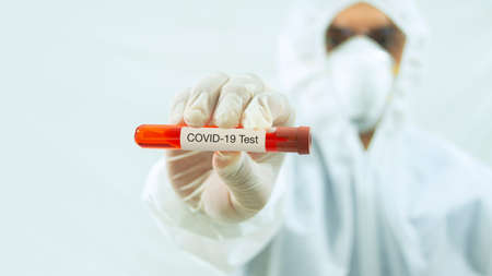 Doctor with mask and white bioprotective suit with arm extended forward and his right hand holding a...