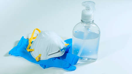 Close up view of plastic bottle with alcohol gel, white face mask and blue latex gloves on white...