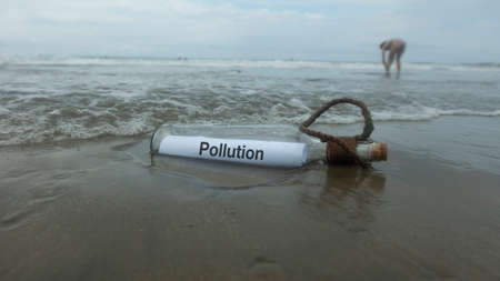 Pollution message inside the glass bottle dragged by the abandoned tide on the beach buried in the sandの写真素材