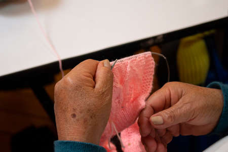 Close up of hands of an old woman with knitting needles knitting a pink wool garment
