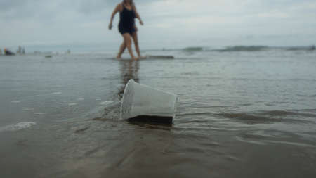 Disposable transparent plastic cup abandoned on the beach dragged by the tide dirtying the sea with...