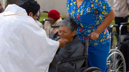 Conocoto, Pichincha / Ecuador - June 12 2019: Catholic priest giving the sacrament of eucharist to...