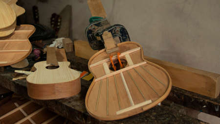 Two wooden guitars in the process of being assembled with presses holding the parts on the...