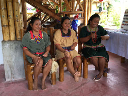 Nueva Loja, Sucumbios / Ecuador - September 2 2020: Group of three indigenous women of Cofan nationality weaving handicrafts in their home in the Amazon rainforestのeditorial素材