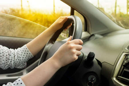Close-up to the hands of a white woman on the steering wheel of a modern car with black upholstery...