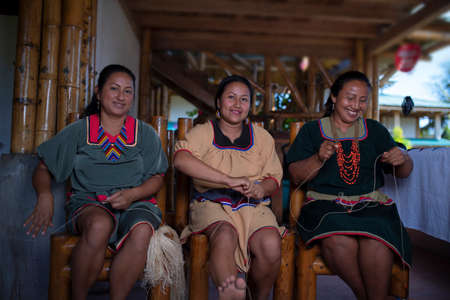 Nueva Loja, Sucumbios / Ecuador - September 2 2020: Indigenous woman of Cofan nationality with green dress smiling while weaving handicrafts sitting on a chair at her home in the Amazon rainforestのeditorial素材