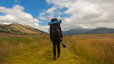 Beautiful Hispanic female explorer seen from behind with backpack walking with a camera in hand in the middle of a sown field on a cloudy morningの写真素材