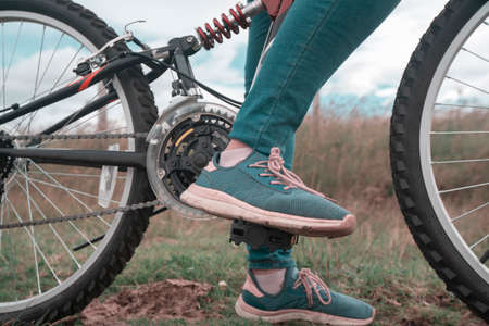 Detail of the feet of a young woman wearing blue pants and blue and pink sports shoes on the pedals...