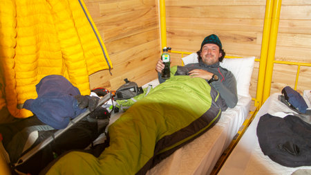 Young climber man resting inside his sleeping bag on a bunk inside a mountain refugeの写真素材