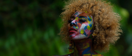 Nueva Loja, Sucumbios / Ecuador - September 3 2020: Portrait of young black woman with colorful painted face with closed eyes with relaxed expression and serenity in a forest with unfocused green backgroundのeditorial素材