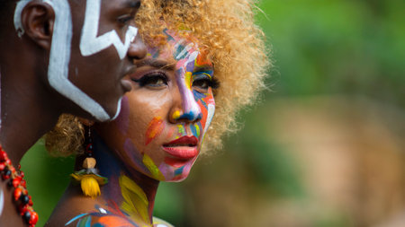 Nueva Loja, Sucumbios / Ecuador - September 3 2020: Profile portrait of young black couple with colorful painted faces with serious expression in a forest with unfocused green backgroundのeditorial素材