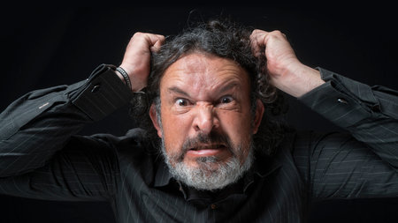 Portrait of latin man with white beard and black curly hair with very angry expression, grabbing his...