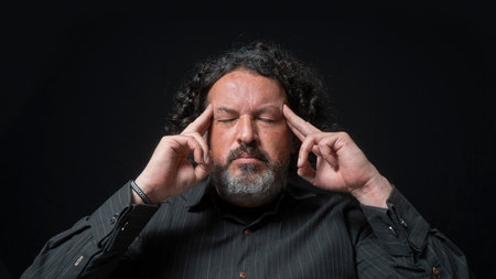 Portrait of latin man with white beard and black curly hair with concentrated expression, with his...