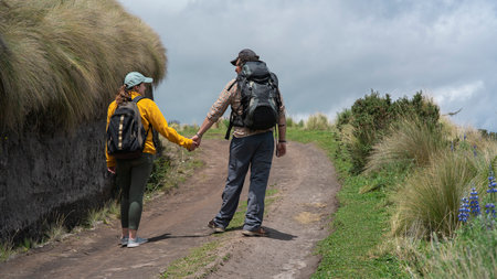 Young Latin American couple with backpacks walking holding hands on a trail in the middle of the...