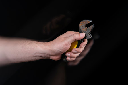 Close-up of man's hand holding a small mechanic's wrench with motion effect against black background