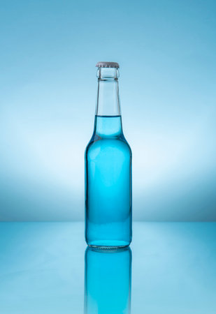 Glass bottle with cap containing blue liquid on reflective blue surface against blue backgroundの写真素材