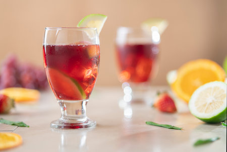 Close-up of glass cups with homemade summer wine in foreground against background of oranges, strawberries and lemons on ceramic tableの写真素材