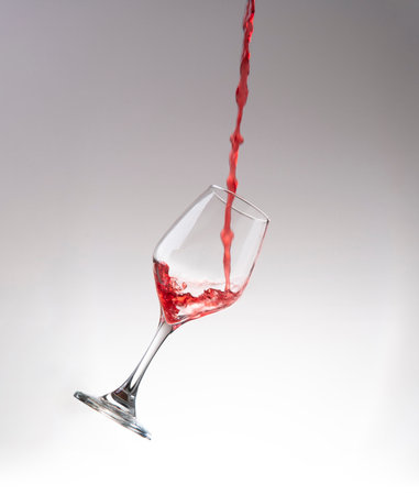 Front view of stream of red wine filling a crystal glass floating in the air against white backgroundの写真素材