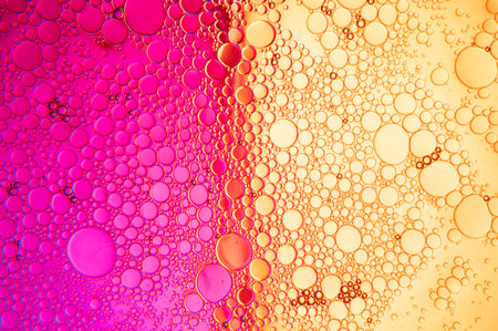 Abstract composition with water and oil drops against a two-tone magenta and orange backgroundの写真素材