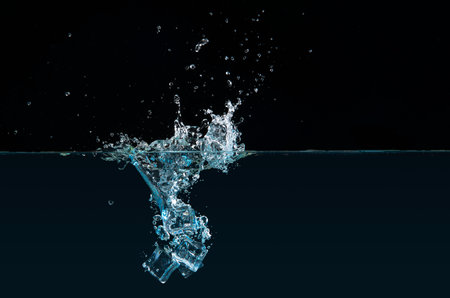 Clear ice cubes dipping into water causing a splash against a black backgroundの写真素材